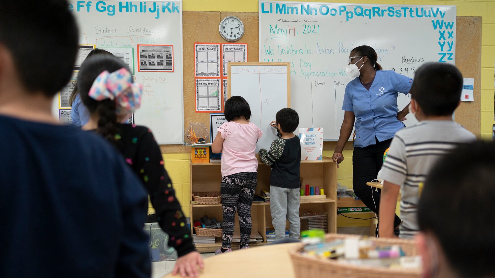 Young students are lined up in front of a white board before participating in a classroom activity.