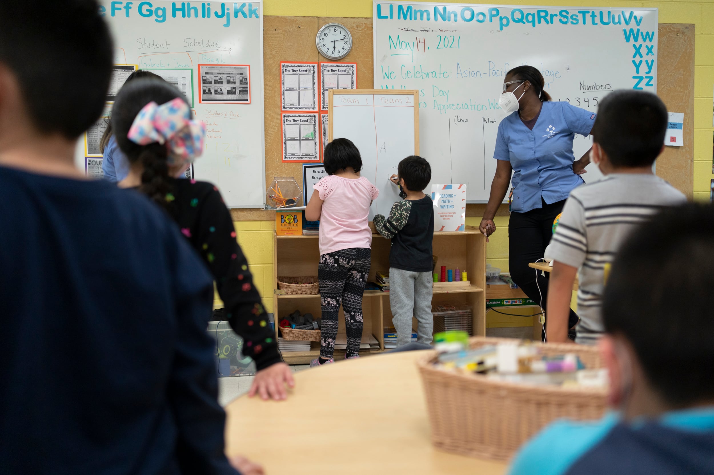 Young students are lined up in front of a white board before participating in a classroom activity.