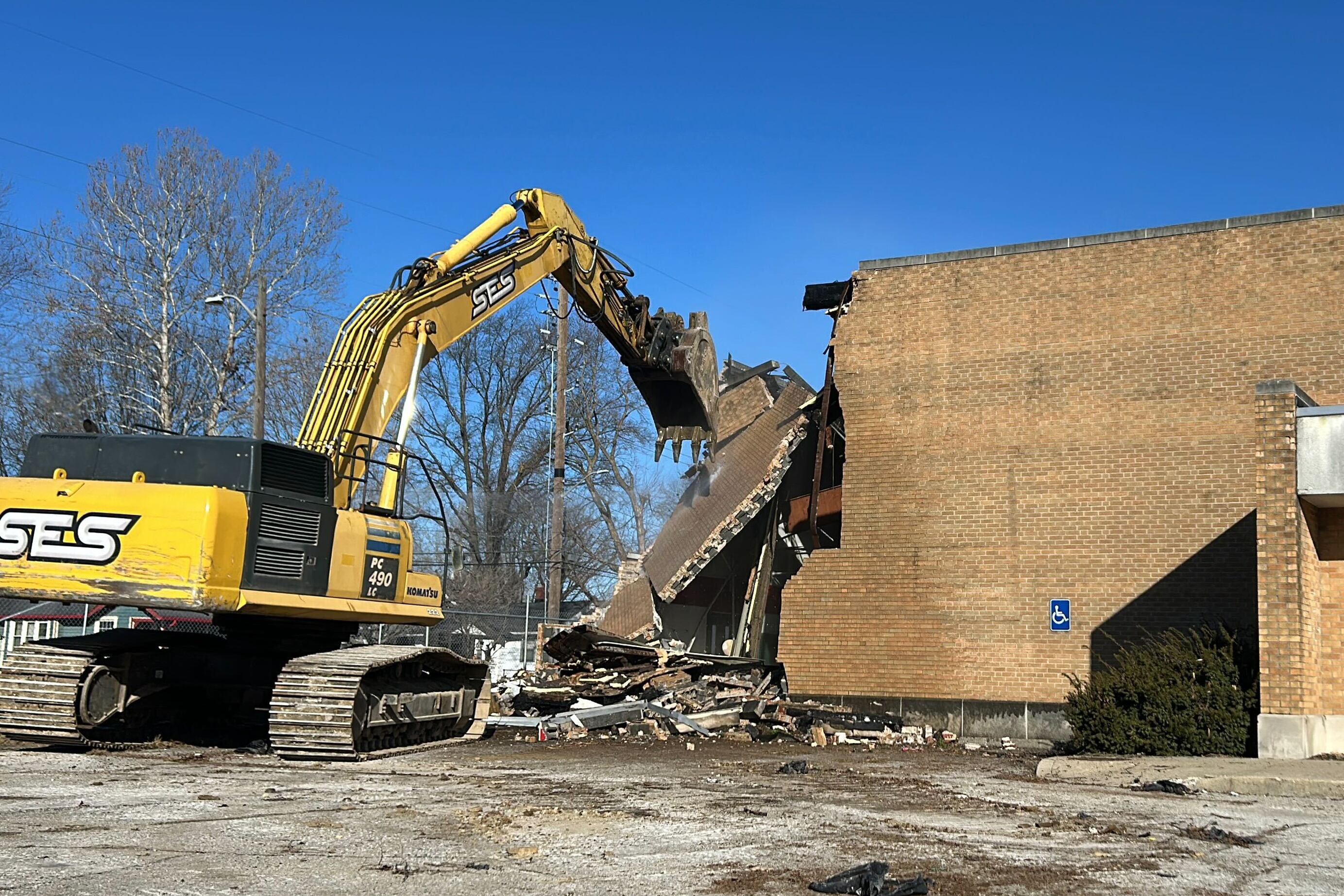 A large yellow and black machine demolishes a brick school building with a blue sky in the background.