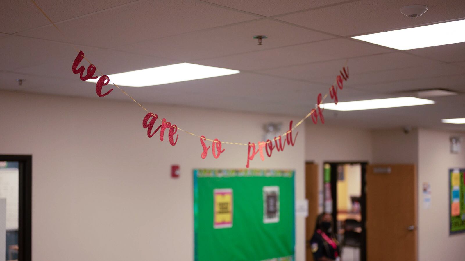 A small string banner that reads “we are so proud of you” hangs in the hallway of a school.