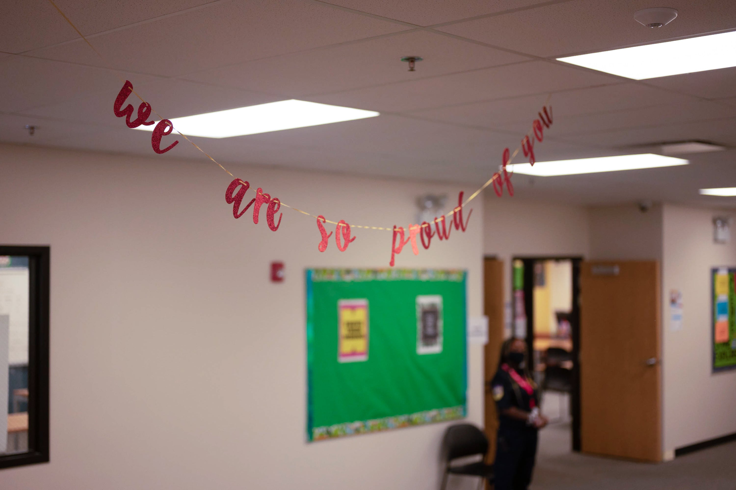 A small string banner that reads “we are so proud of you” hangs in the hallway of a school.