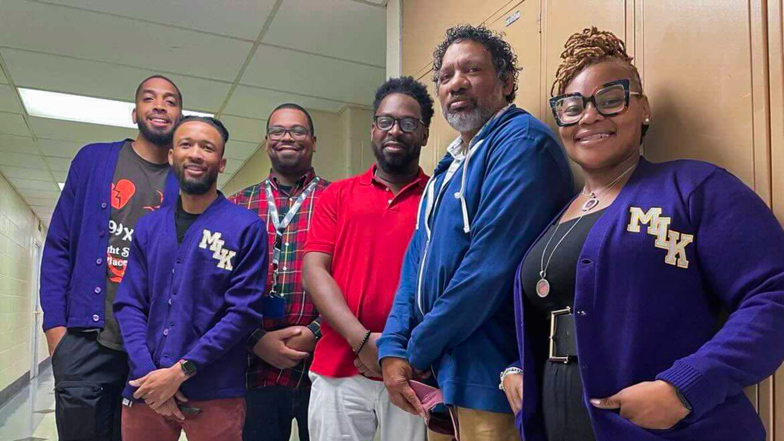 Five men stand to the right of one woman in a hallway. The woman is wearing a shirt that has “MLK” on it.