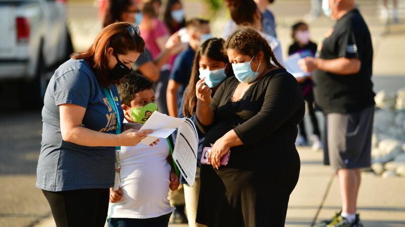 Teachers, students, and parents with masks on outside a school.