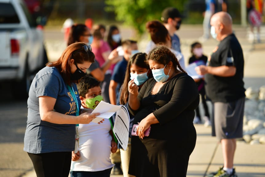 Teachers, students, and parents with masks on outside a school.