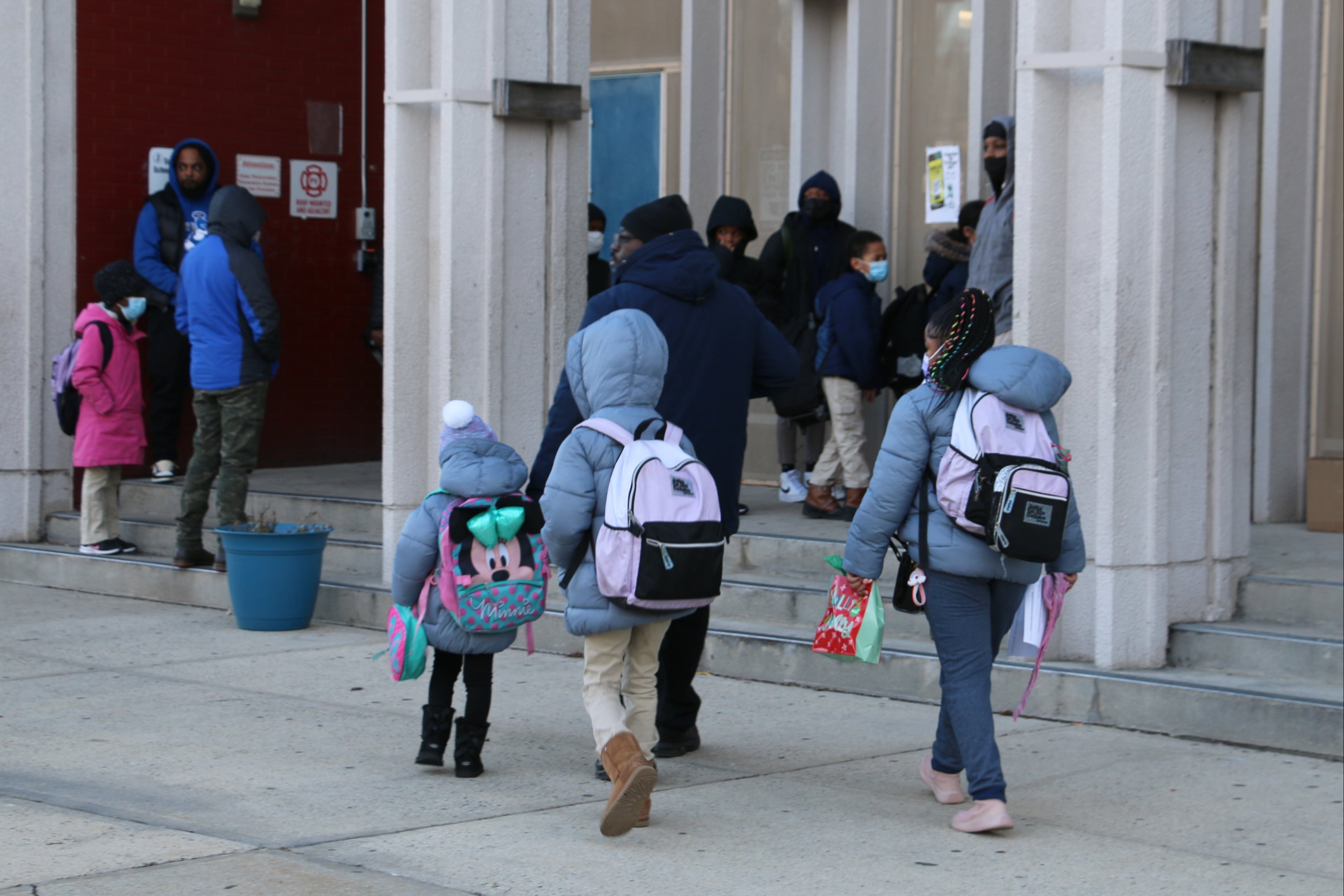 Children, wearing winter jackets and carrying backpacks, walk into Camden Street Elementary School.