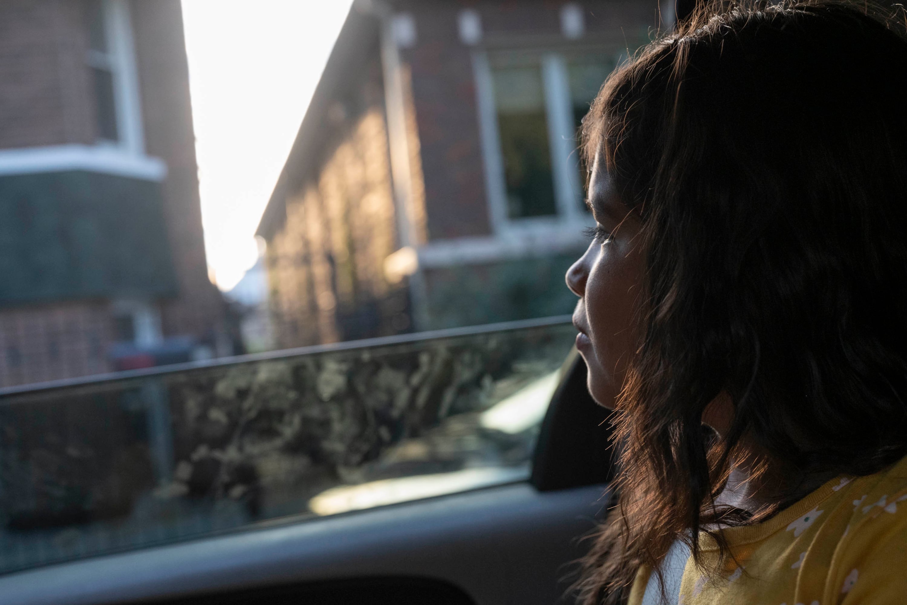 A young girl looks out the window of a car as early morning light outlines her face.