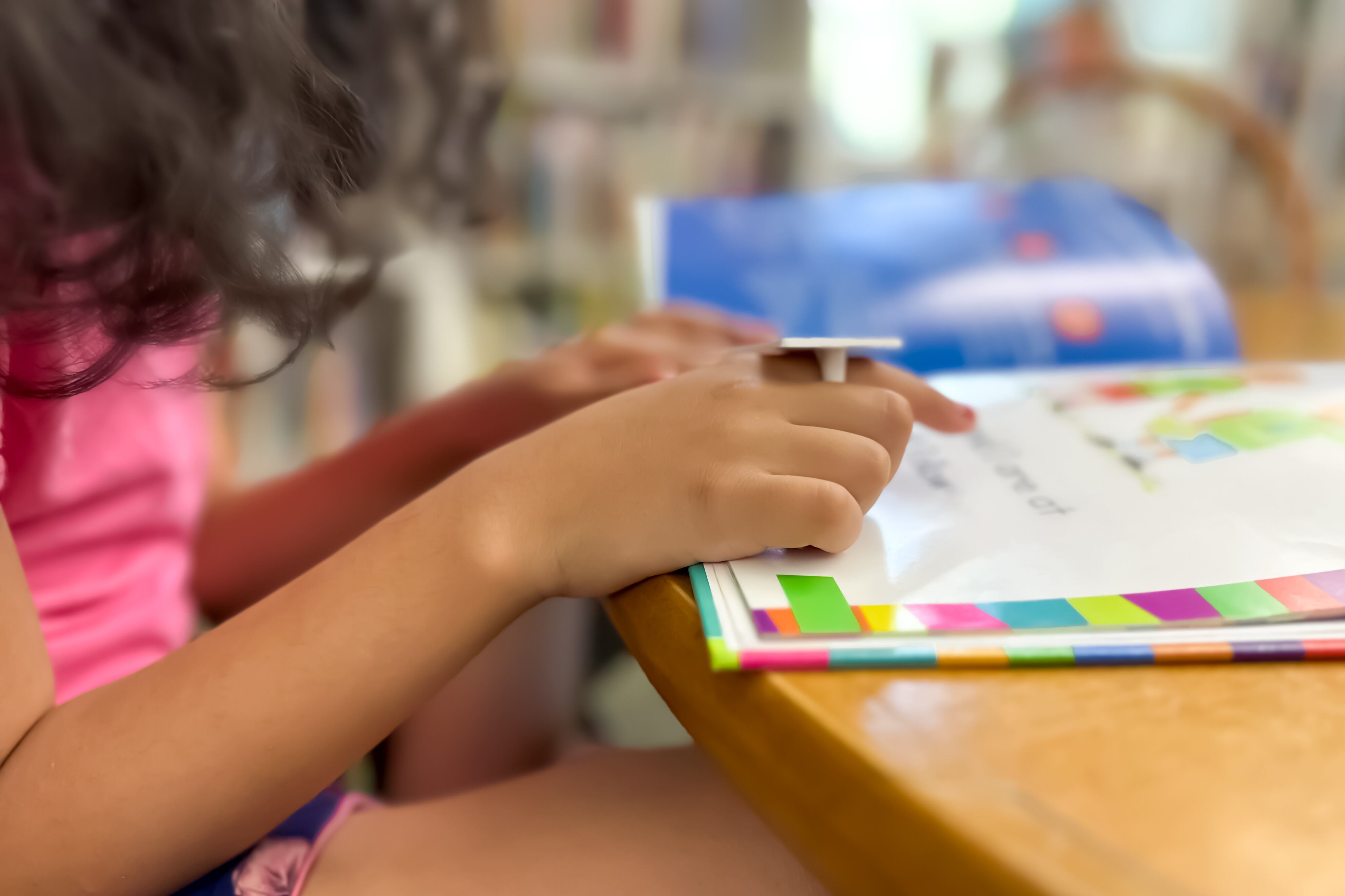 A girl in a pink top points at a book.