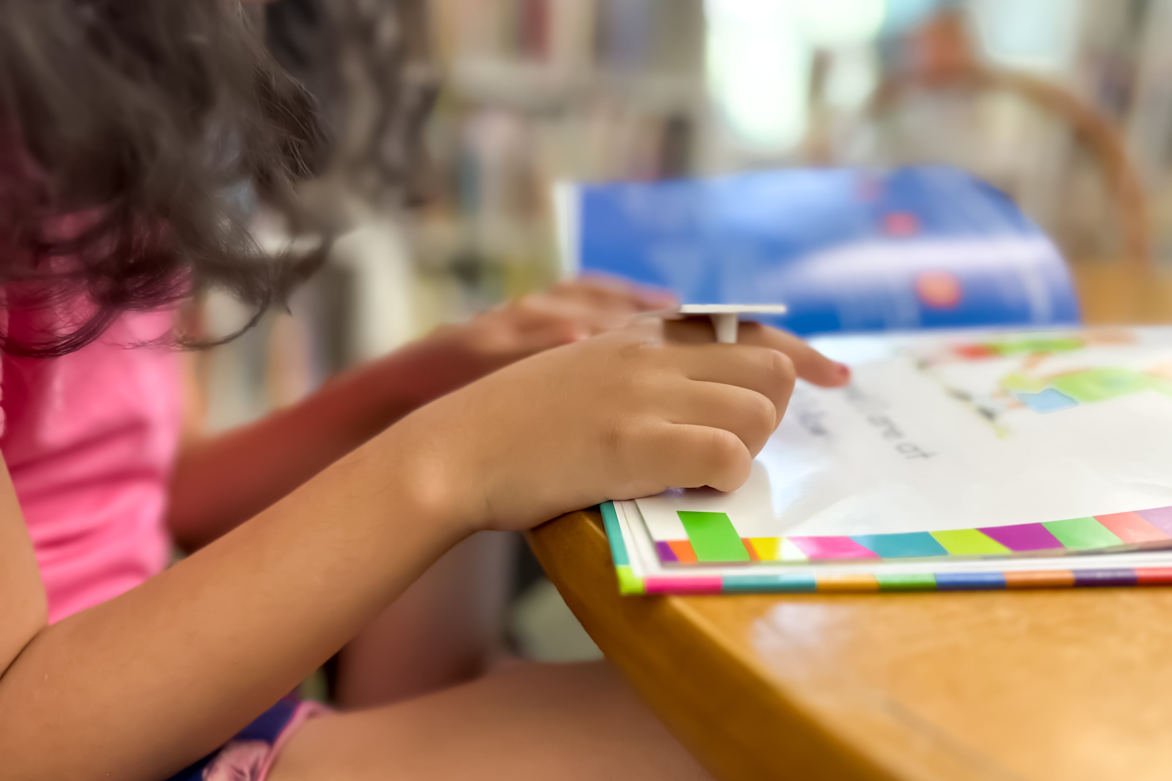 A girl in a pink top points at a book.