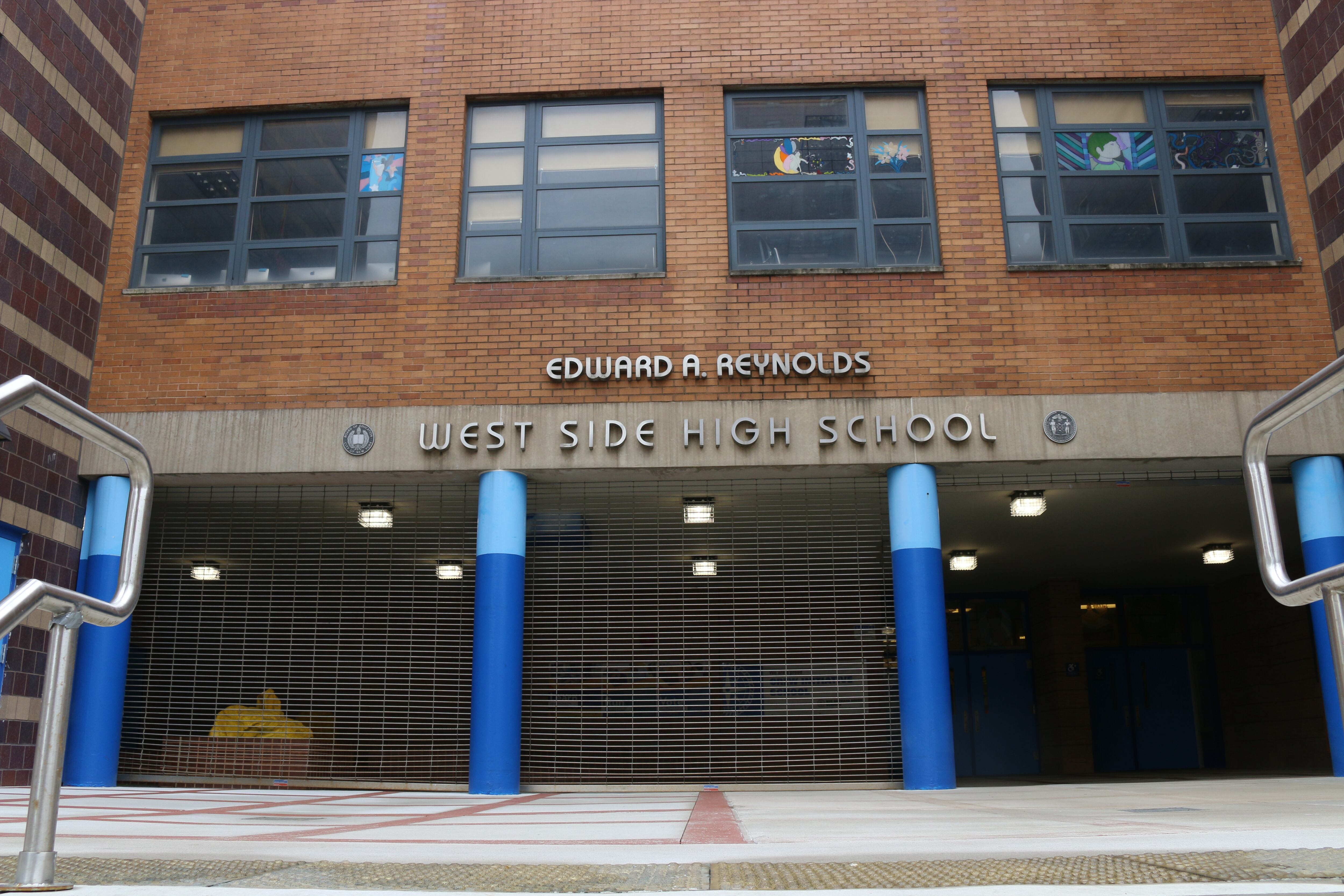 A brick building with blue columns and a sign that reads "West Side High School" on the top.