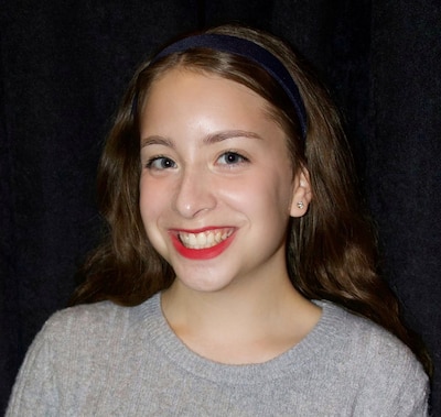A headshot of a teenage girl with dark blond hair. She is wearing a grey sweater.