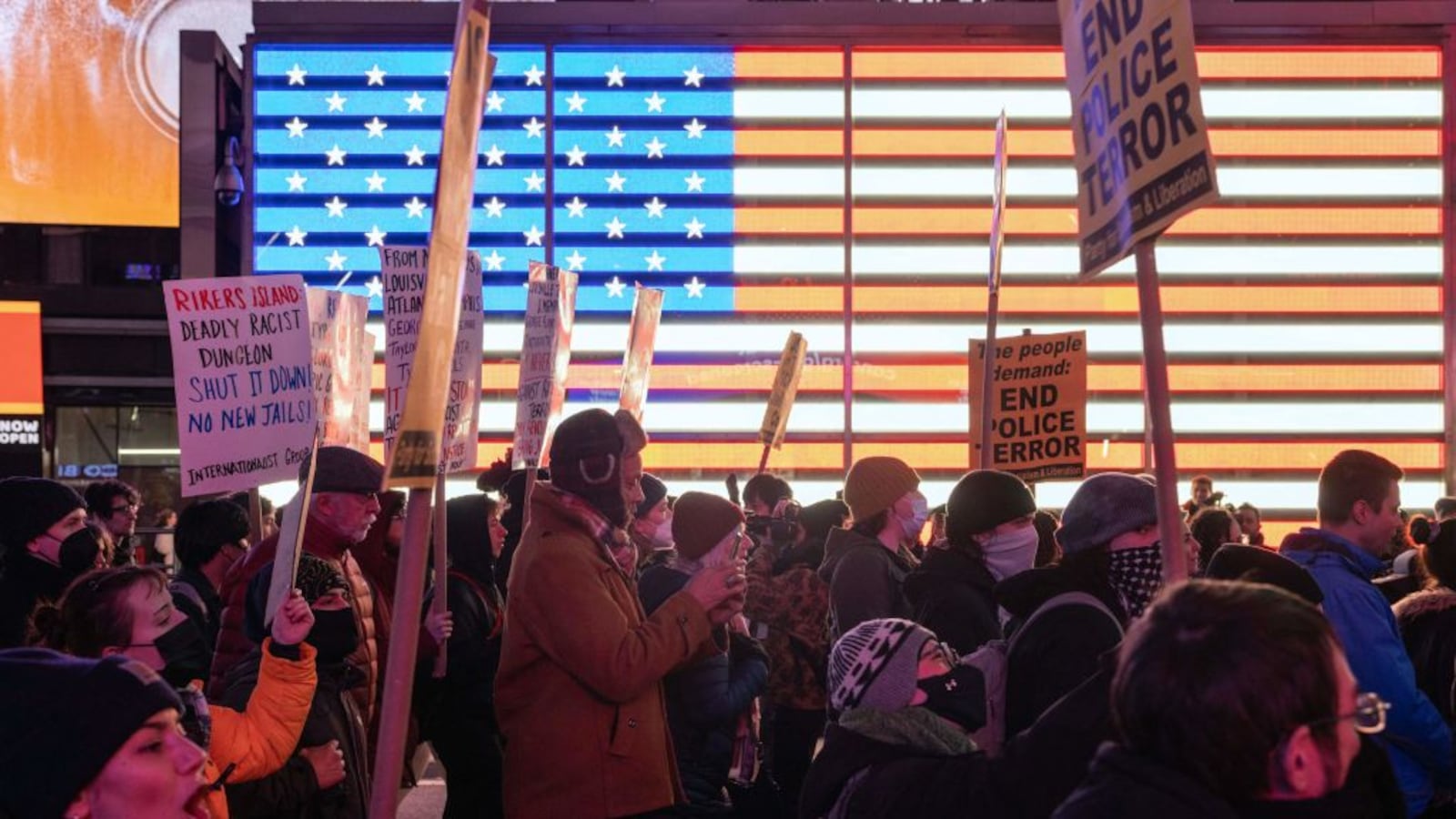 Protesters in Times Square rally against police violence and prison conditions. A digital Americna flag is in the background. 