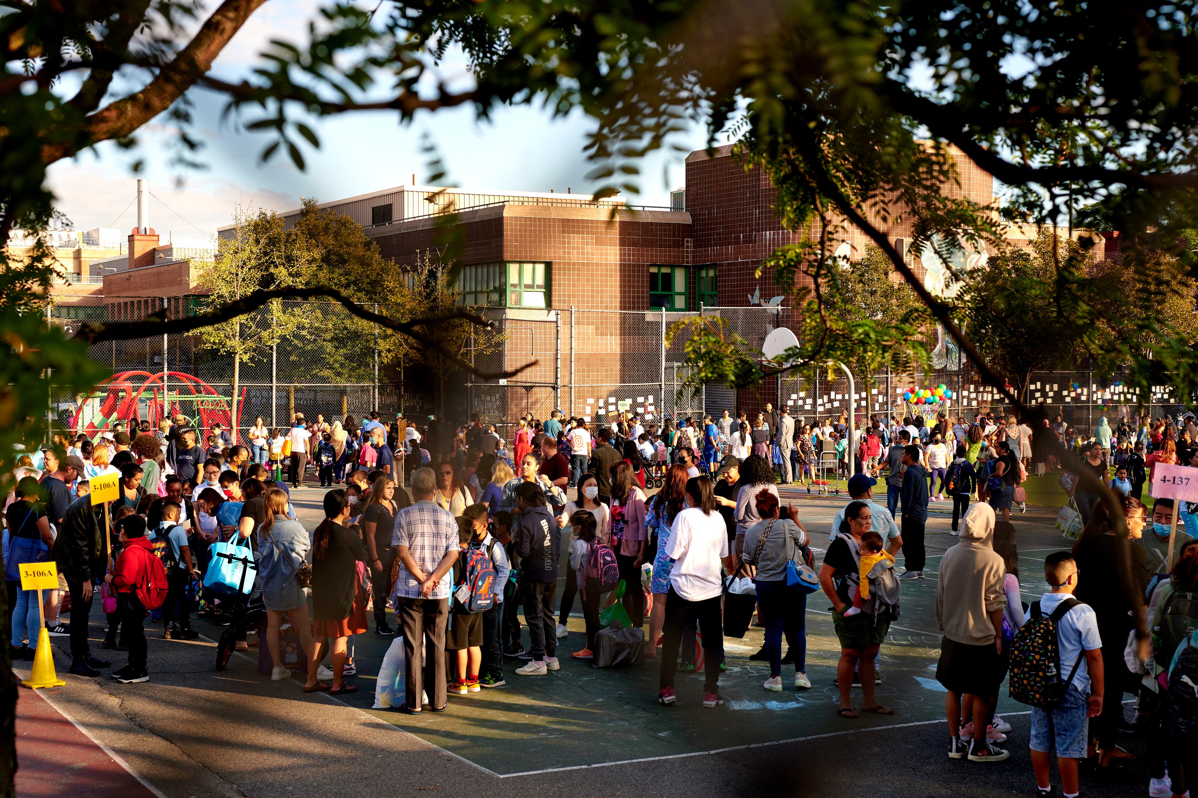 Scores of parents and their children stand on a school blacktop on the first day of classes.