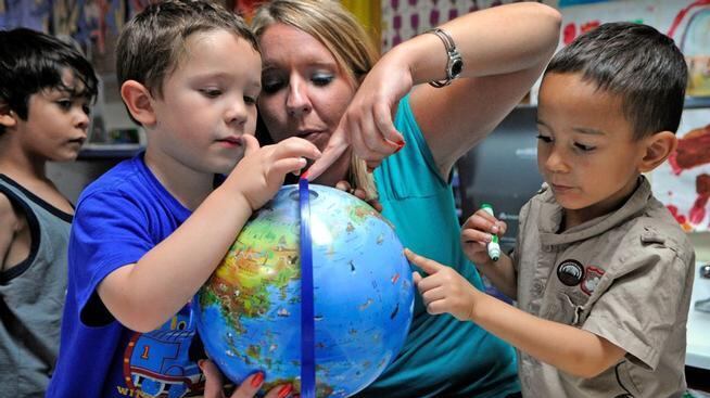 A woman and two young boys point to places on a globe.