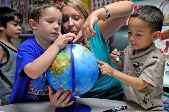 A woman and two young boys point to places on a globe.