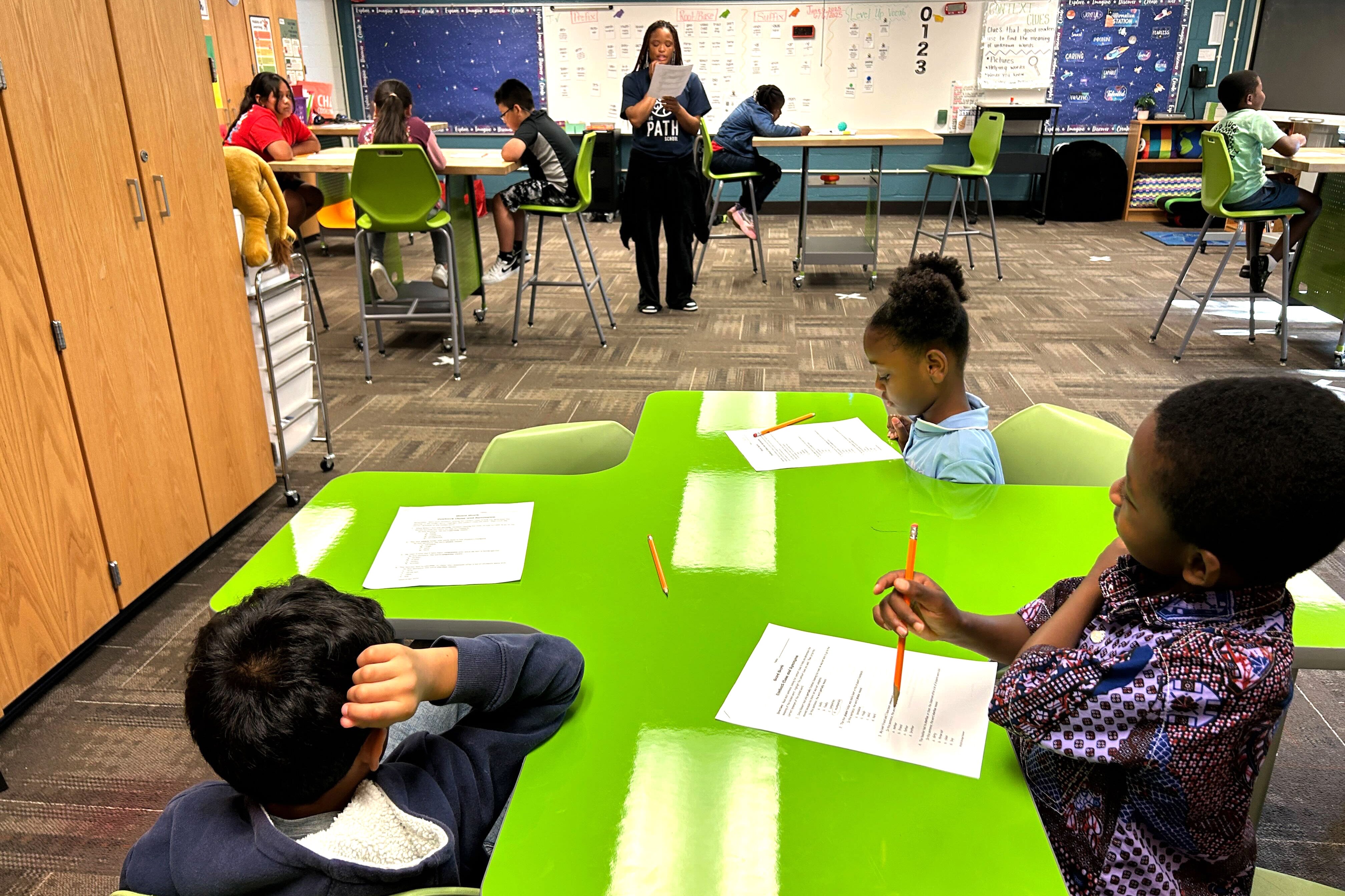Students sit at a green table in a classroom.
