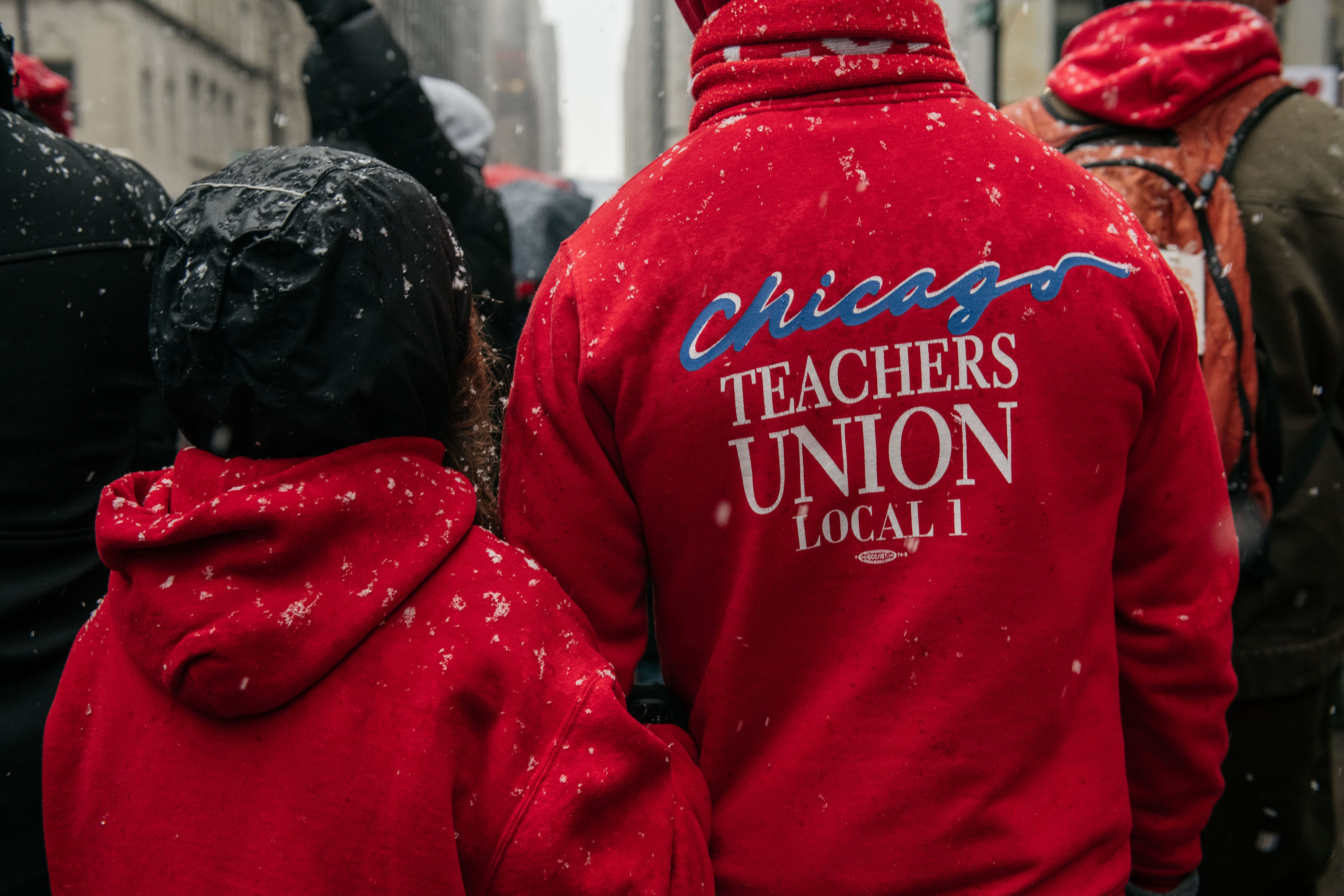 Chicago Teachers Union members stand with their backs to the camera, wearing red jackets with the union’s name.