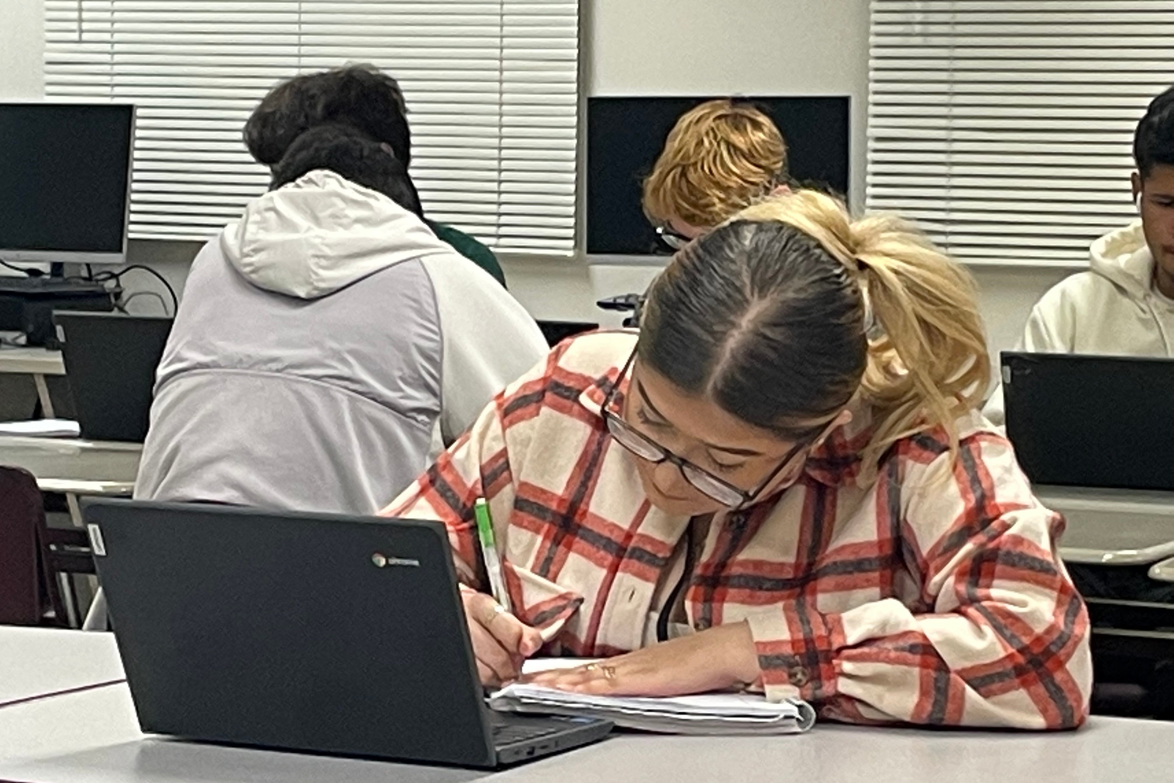 A high school girl looks down at a notebook she’s writing in.