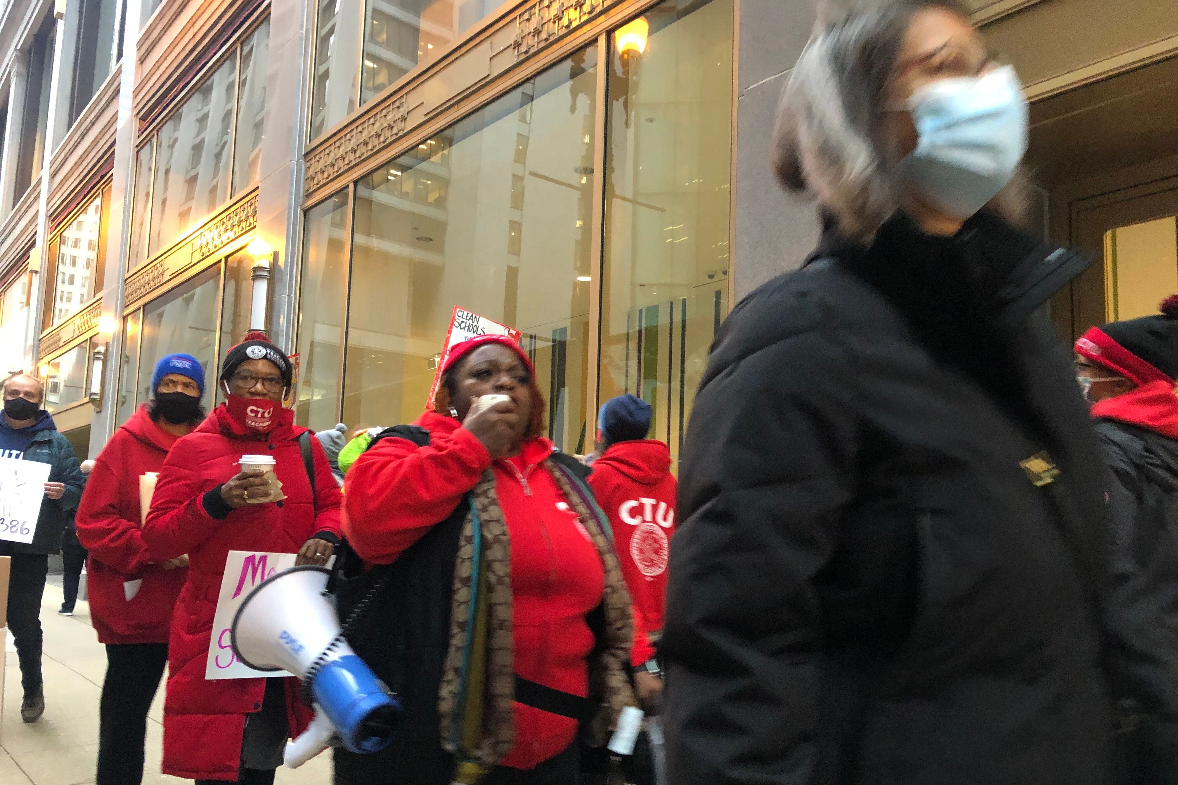 A group of people wearing red carrying posters and a megaphone march on a downtown sidewalk.