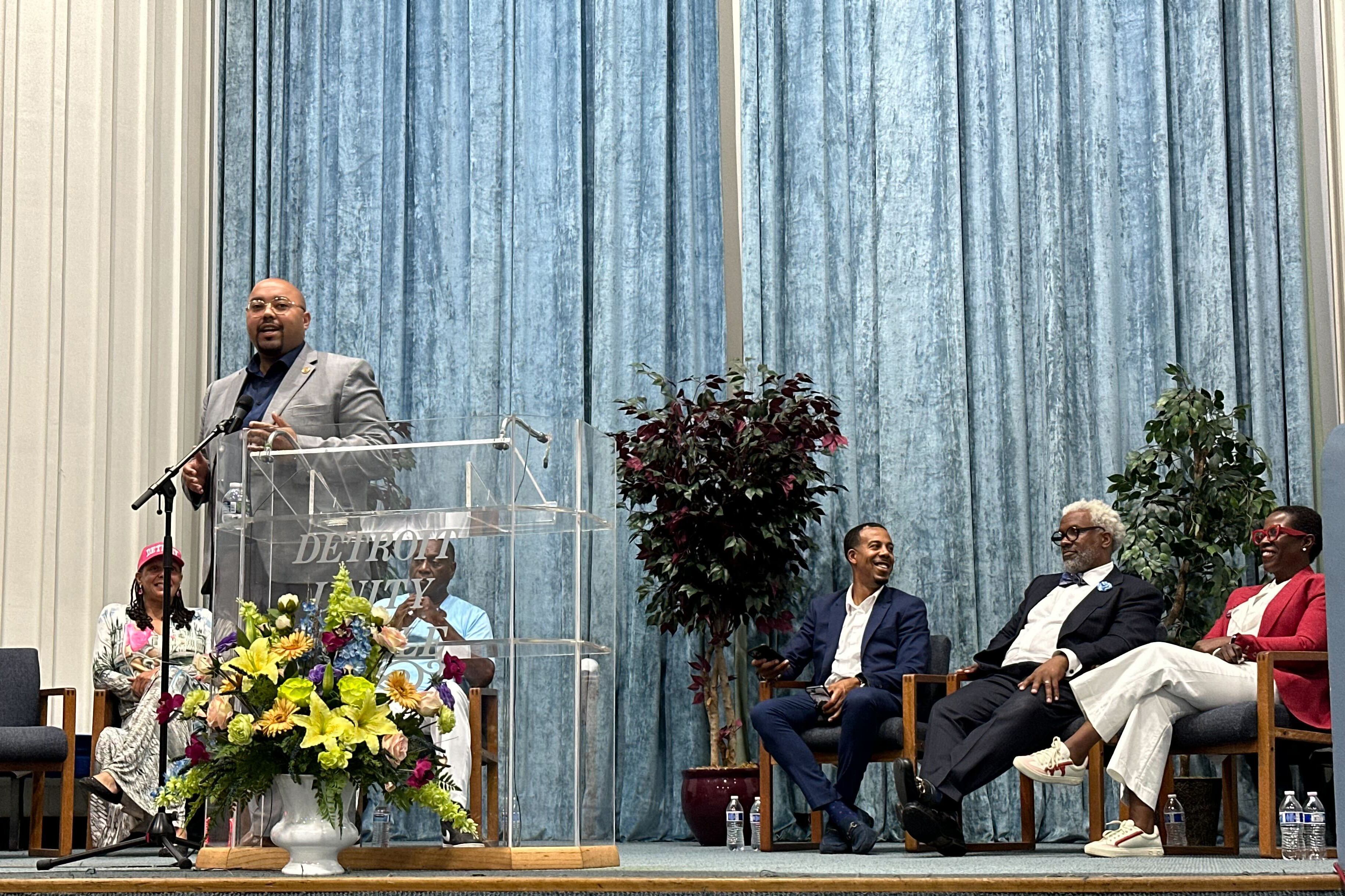 A photograph of six adults in business attire on stage during a forum.