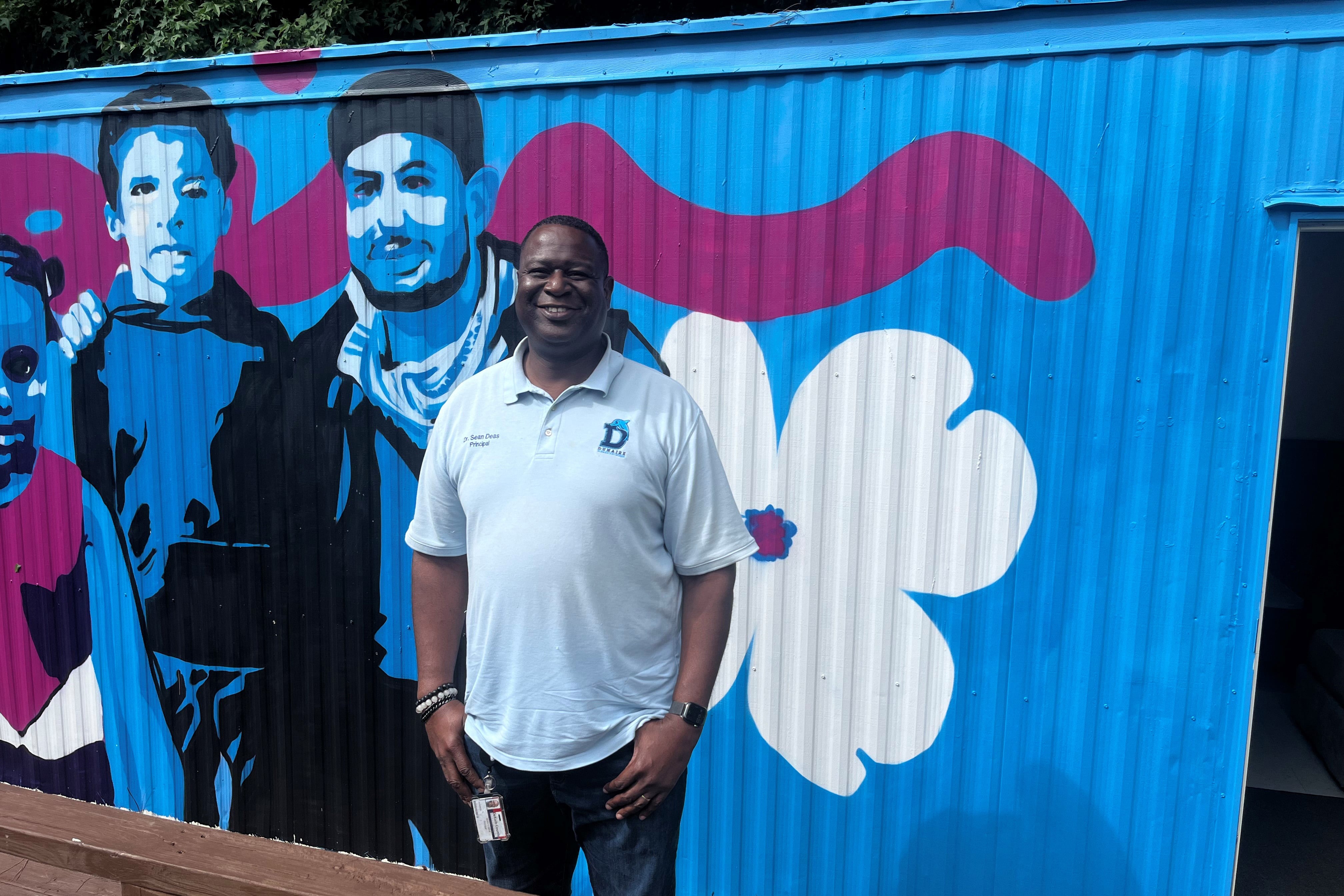 School Principal Sean Deas stands in front of a colorful mural.