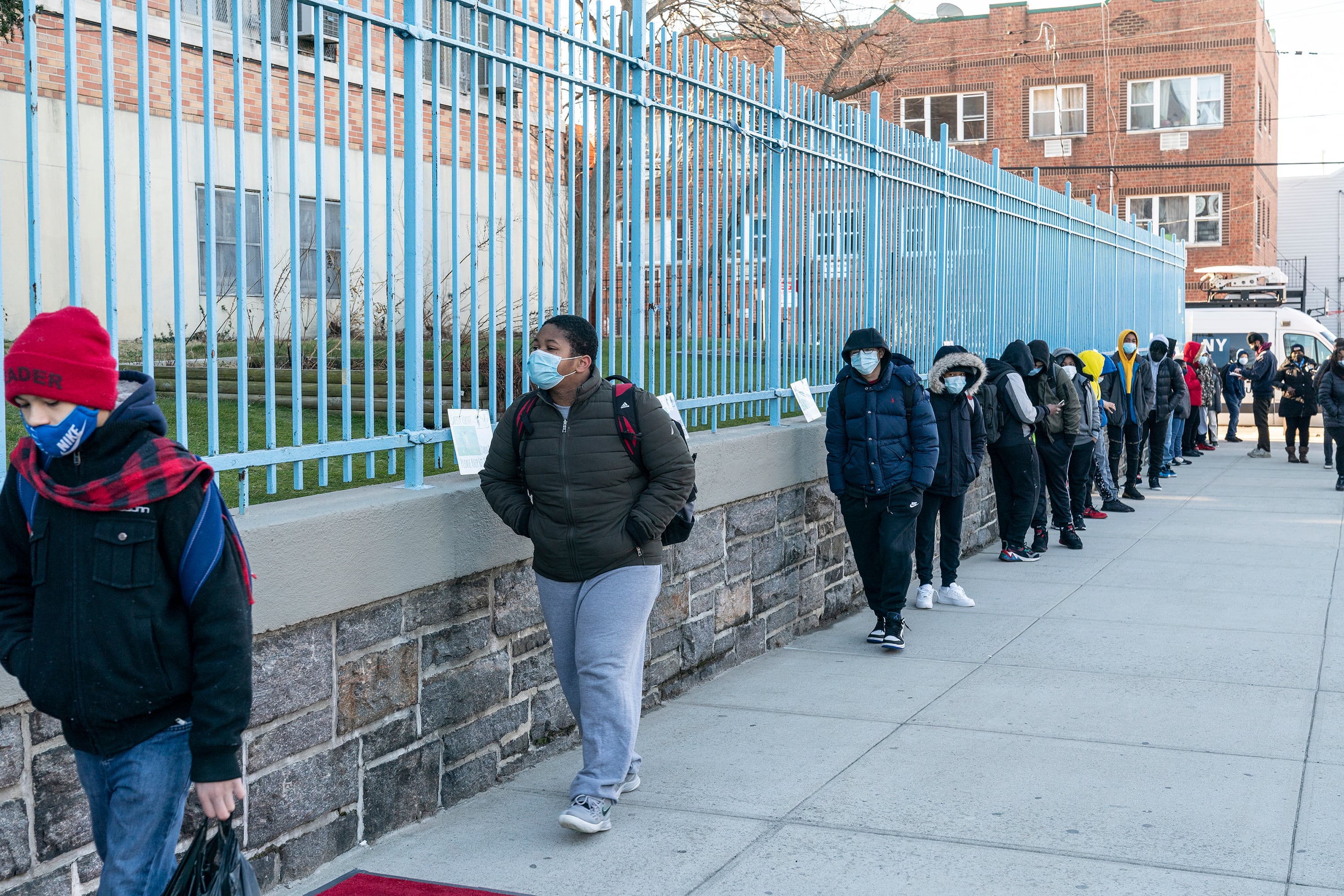 Middle school students line up outside of their school’s fence as they return to school, all wearing protective masks.