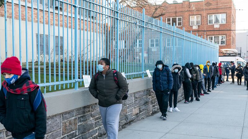 Middle school students line up outside of their school’s fence as they return to school, all wearing protective masks.