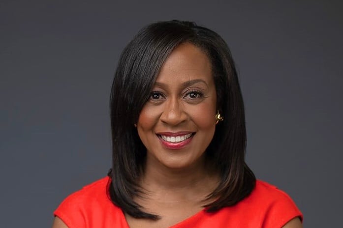 A woman wearing a red dress smiles for the camera in front of a grey backdrop