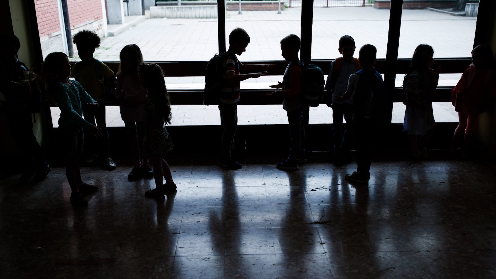 A large group of students speak together in a hallway, silhouetted against a window.