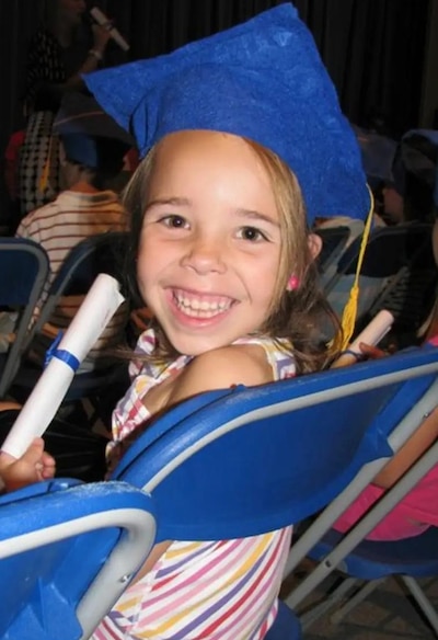 A child in a graduation cap holds diploma during a kindergarten graduation ceremony.