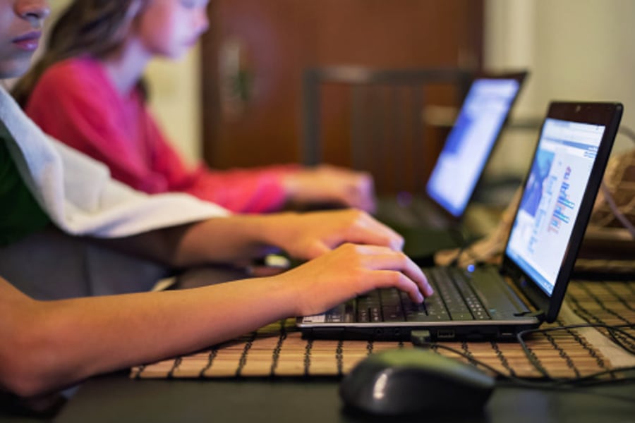 A photograph of students' arms reaching out to type on a keyboard in a classroom.