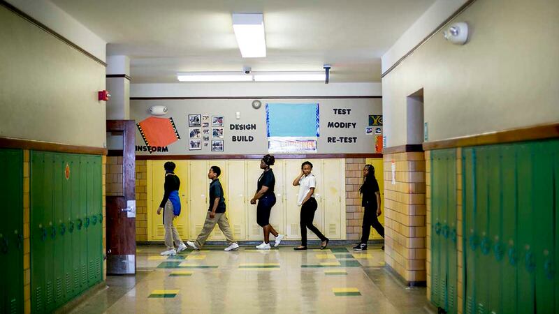 Students walk down a hallway during class change. The walls are lined with green and yellow lockers.