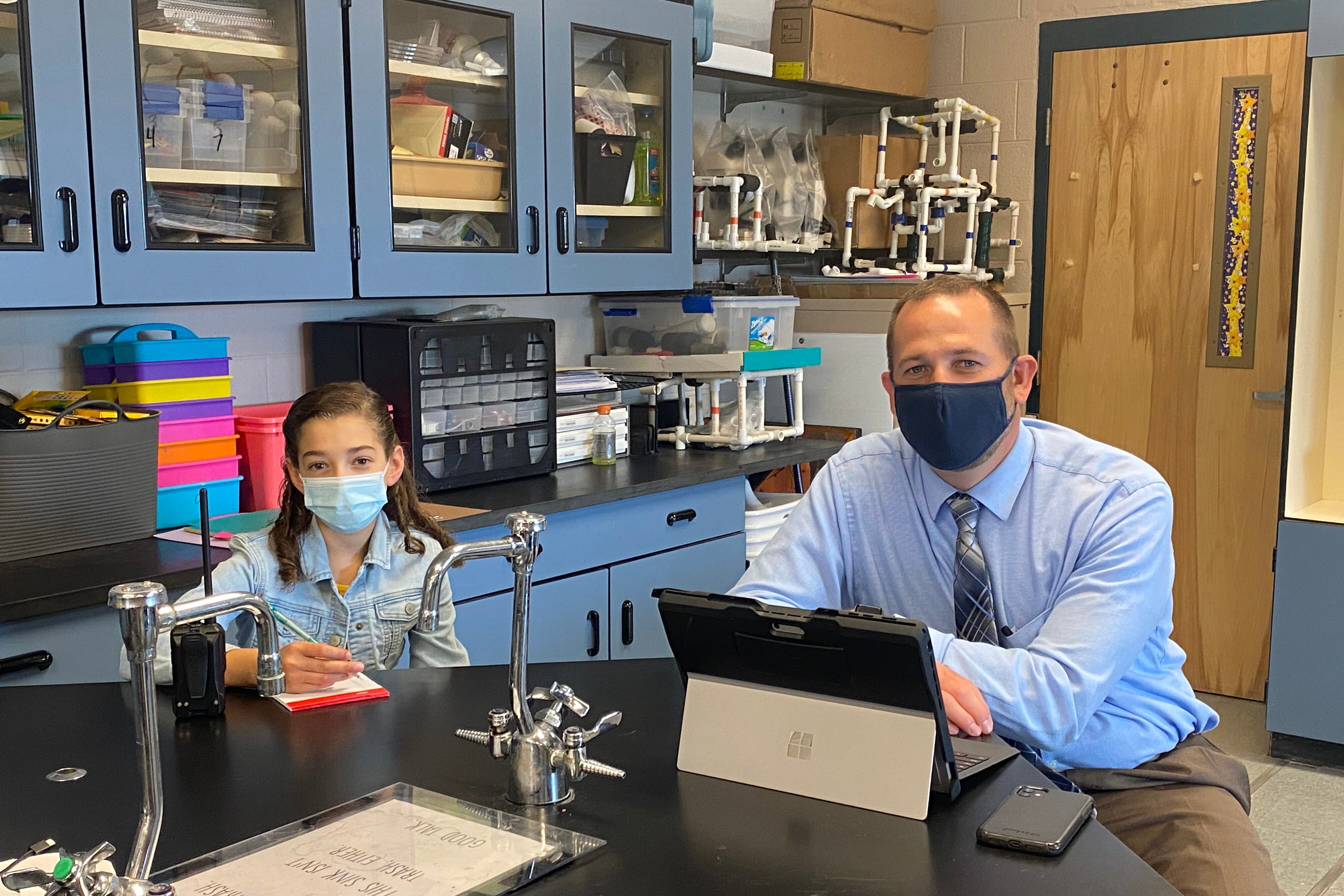 A young student and an adult sit at a school table.
