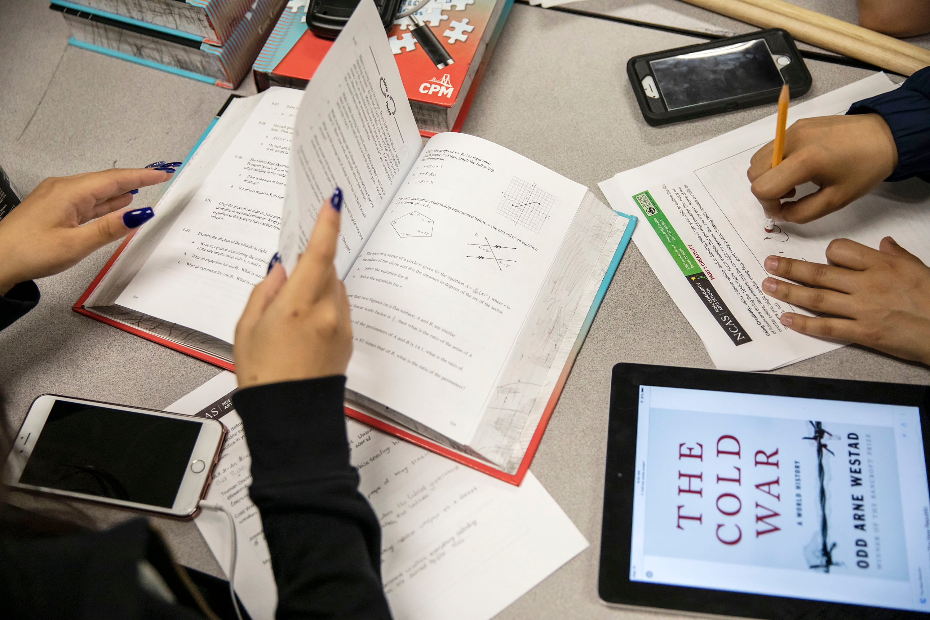 Two students pairs of hands look through textbooks on top of a table in a classroom.