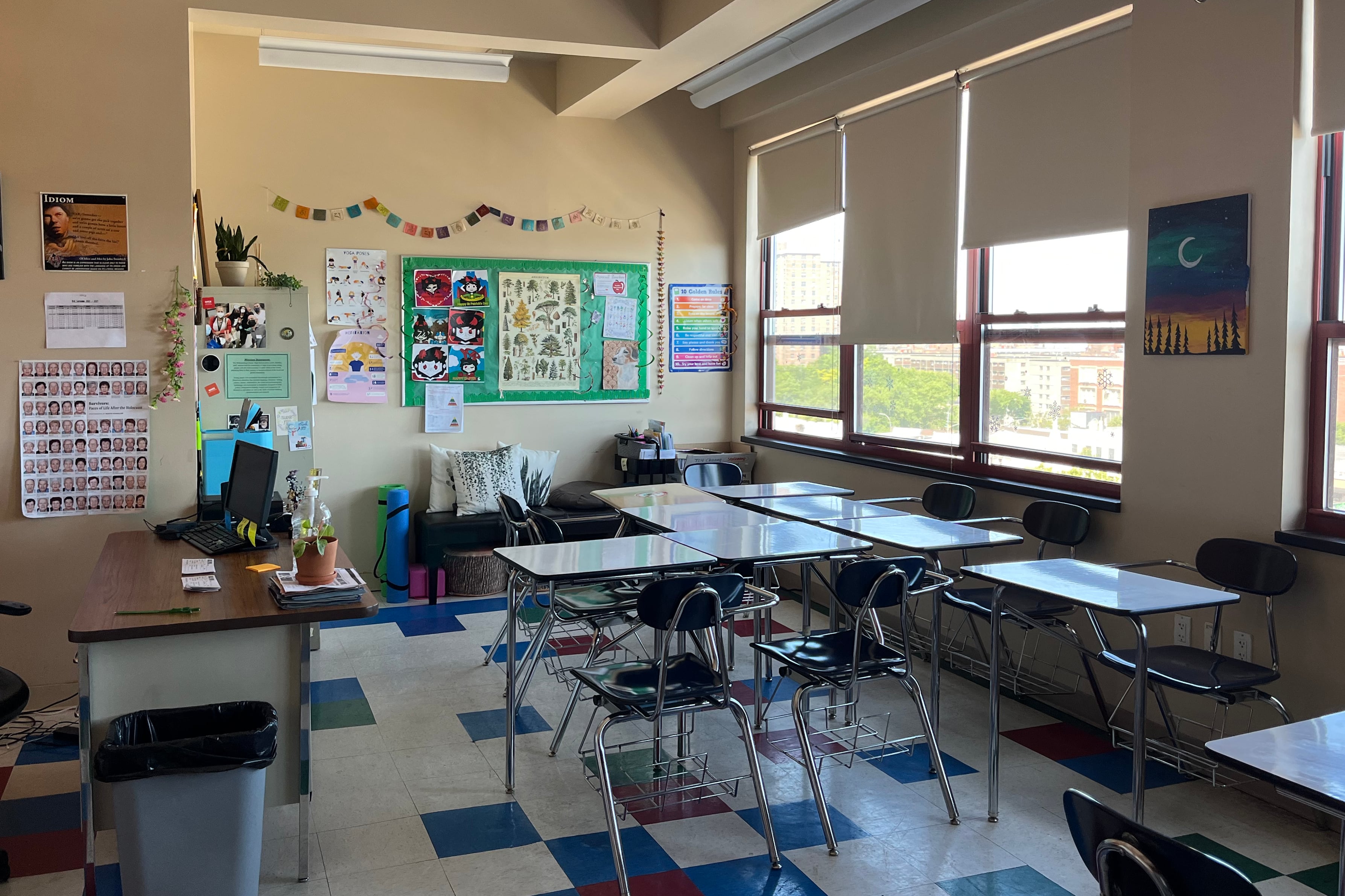 The interior of a school classroom, with empty desks and chairs. Lights are off. No people present.