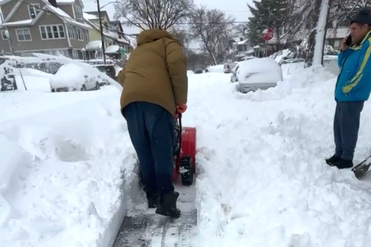 A man in a brown jacket shovels snow.