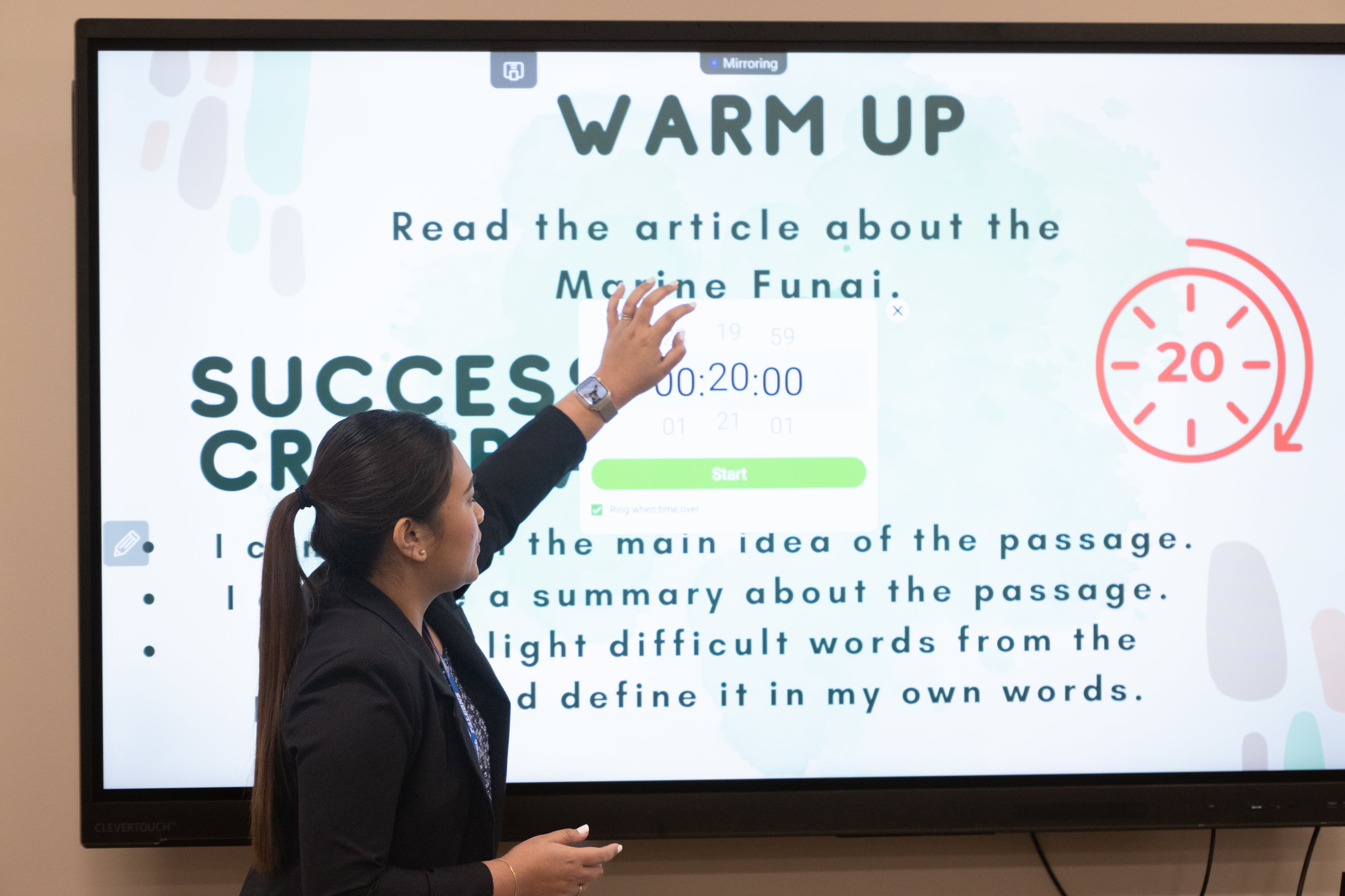 A woman with dark hair points to a screen in a school