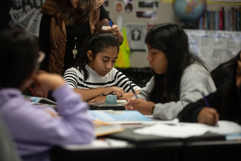 A female student in a striped top and a female student with a light gray top work at a table.