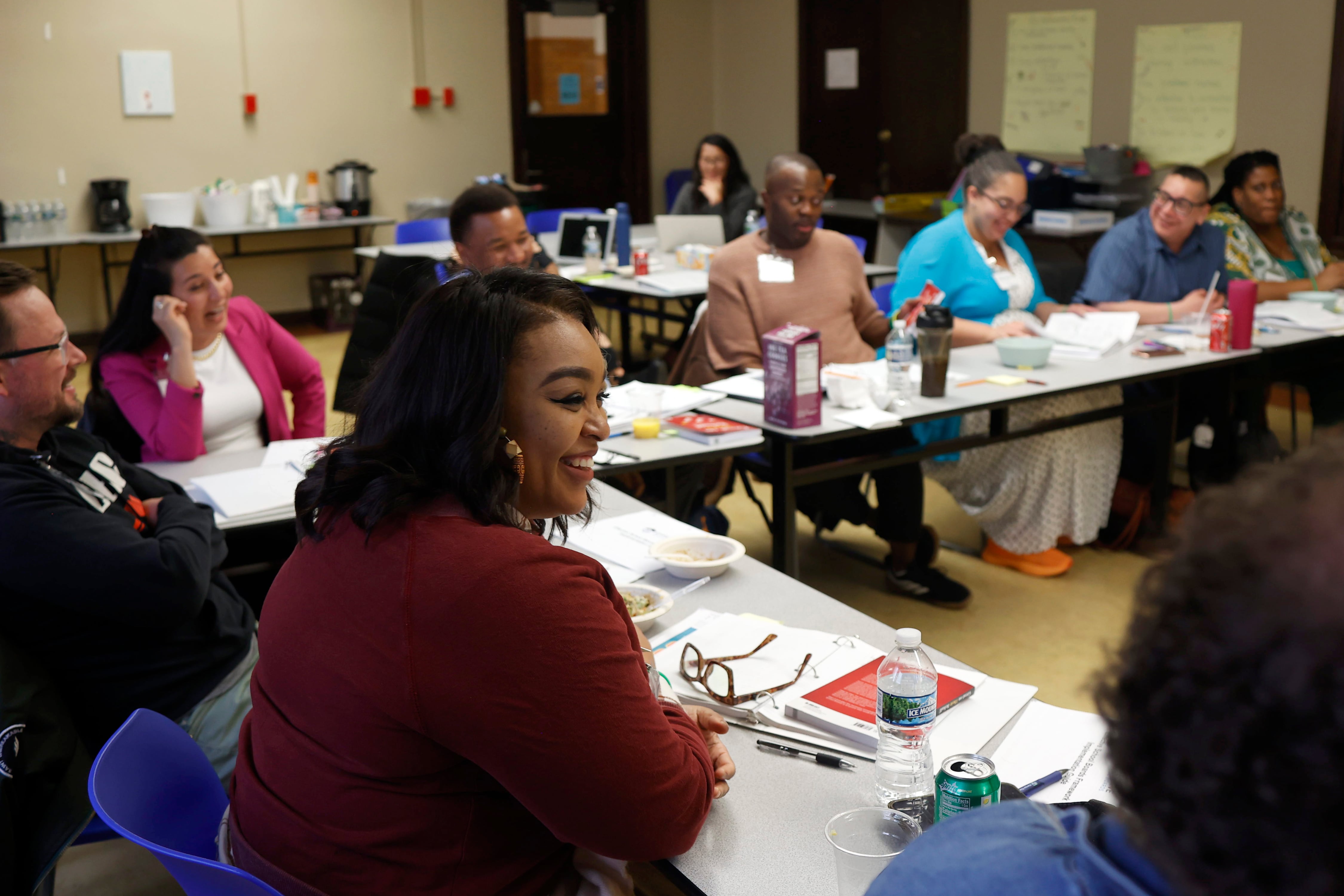 A large group of people sit at a table with notebooks and water bottles in a classroom.
