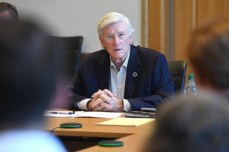 A man with white hair in a suit sits at a table.