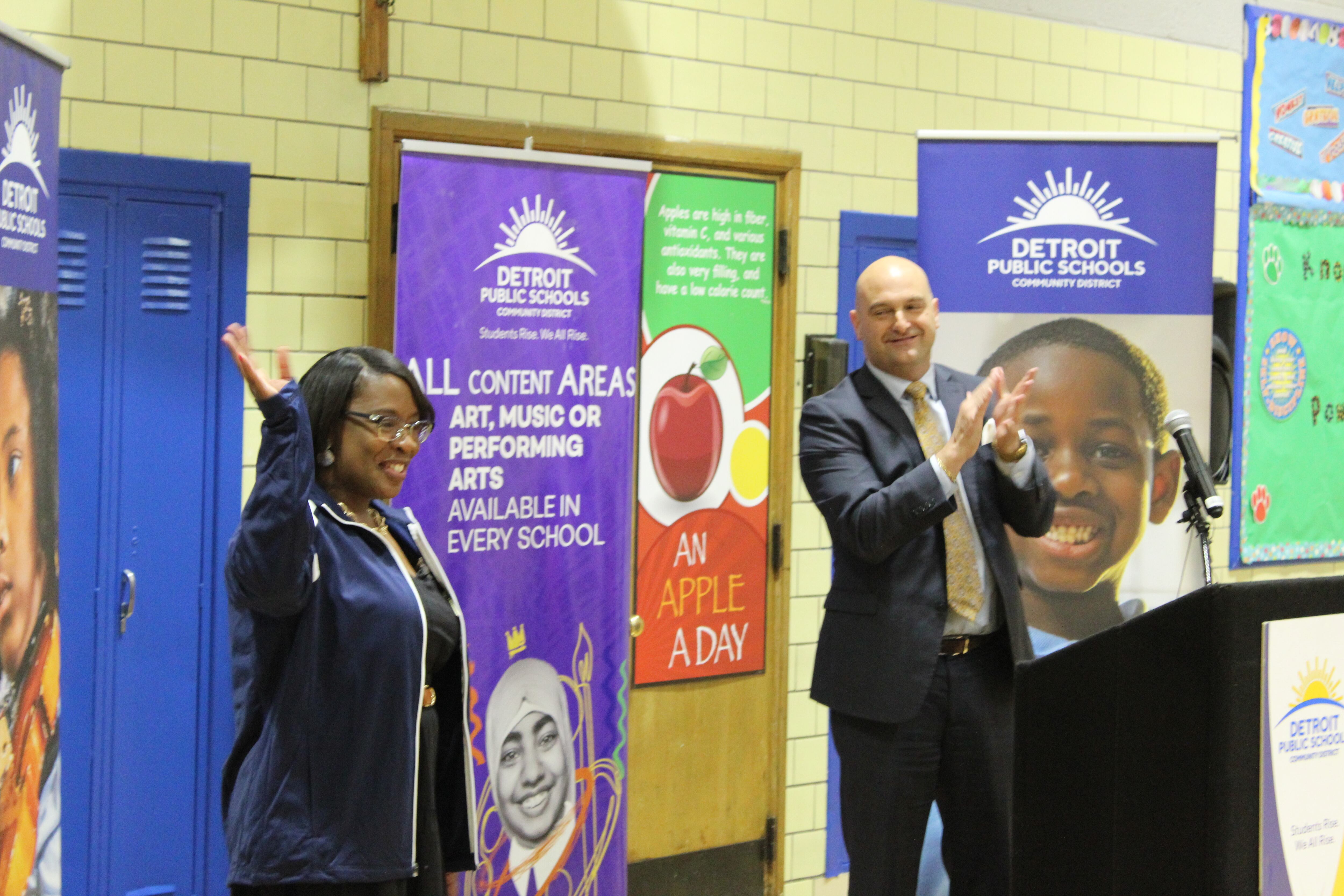 A teacher waves to applause as she is honored at a ceremony.