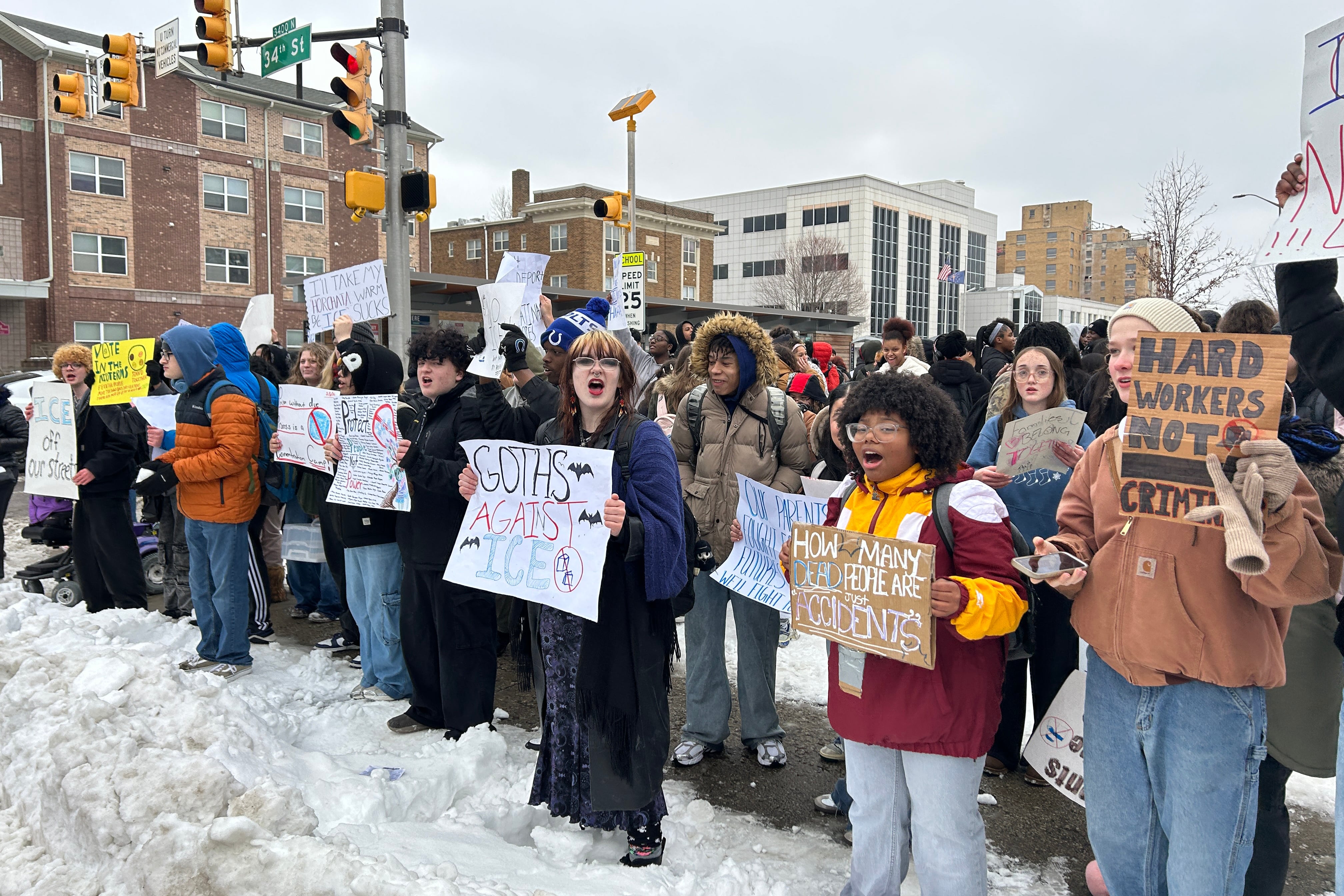 A photograph of a large group of high school students, some holding protest signs and all dressed in coats and cold weather gear stand outside on a cold, cloudy day protesting against ICE.