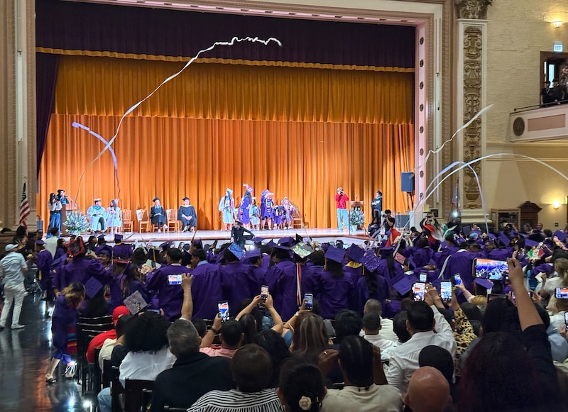 A photograph of people celebrating in a high school auditorium with a large audience.