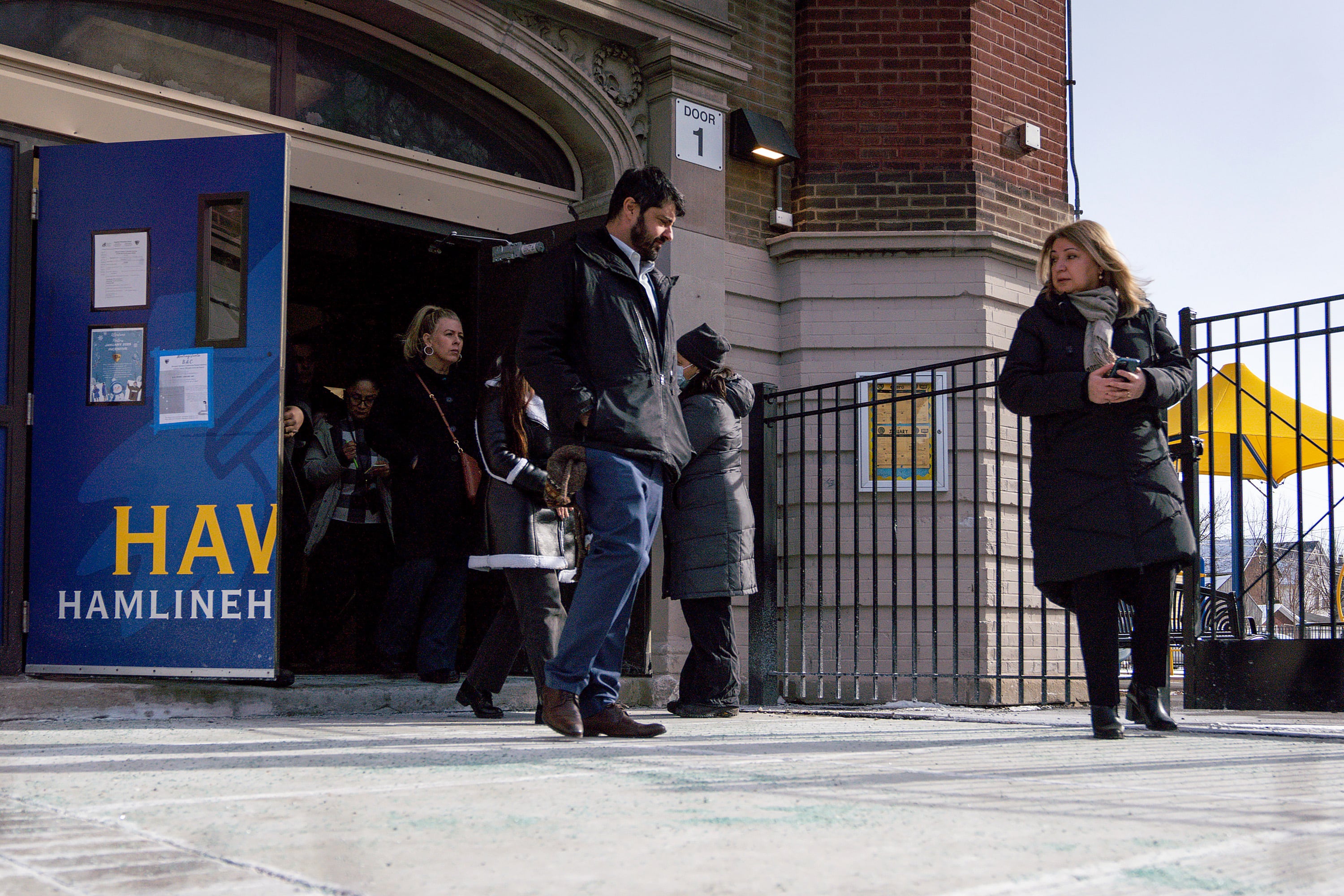 Adults in jackets walk out of an elementary school entrance.