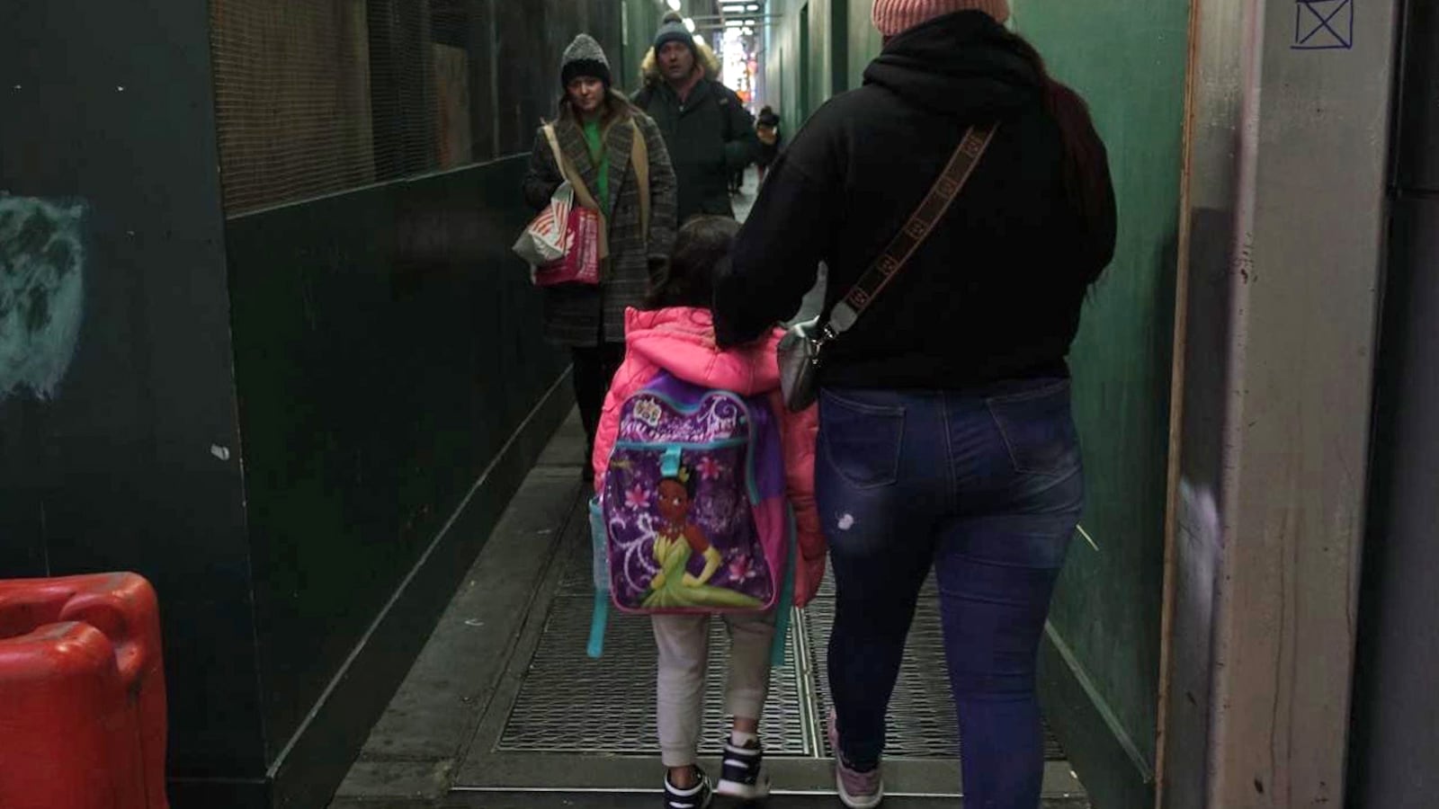 An adult and a child walk away from the camera down an aisle with green walls.