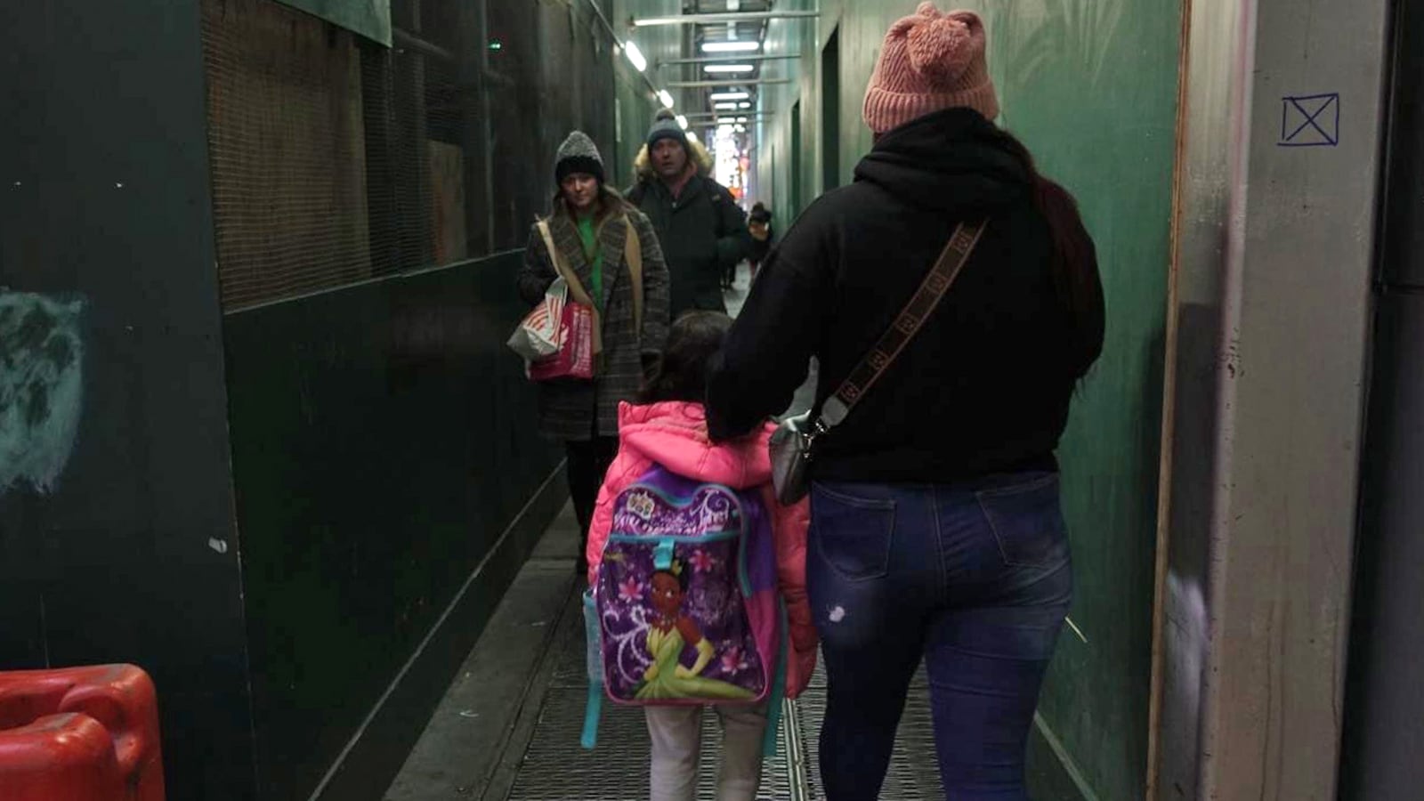 An adult and a child walk away from the camera down an aisle with green walls.