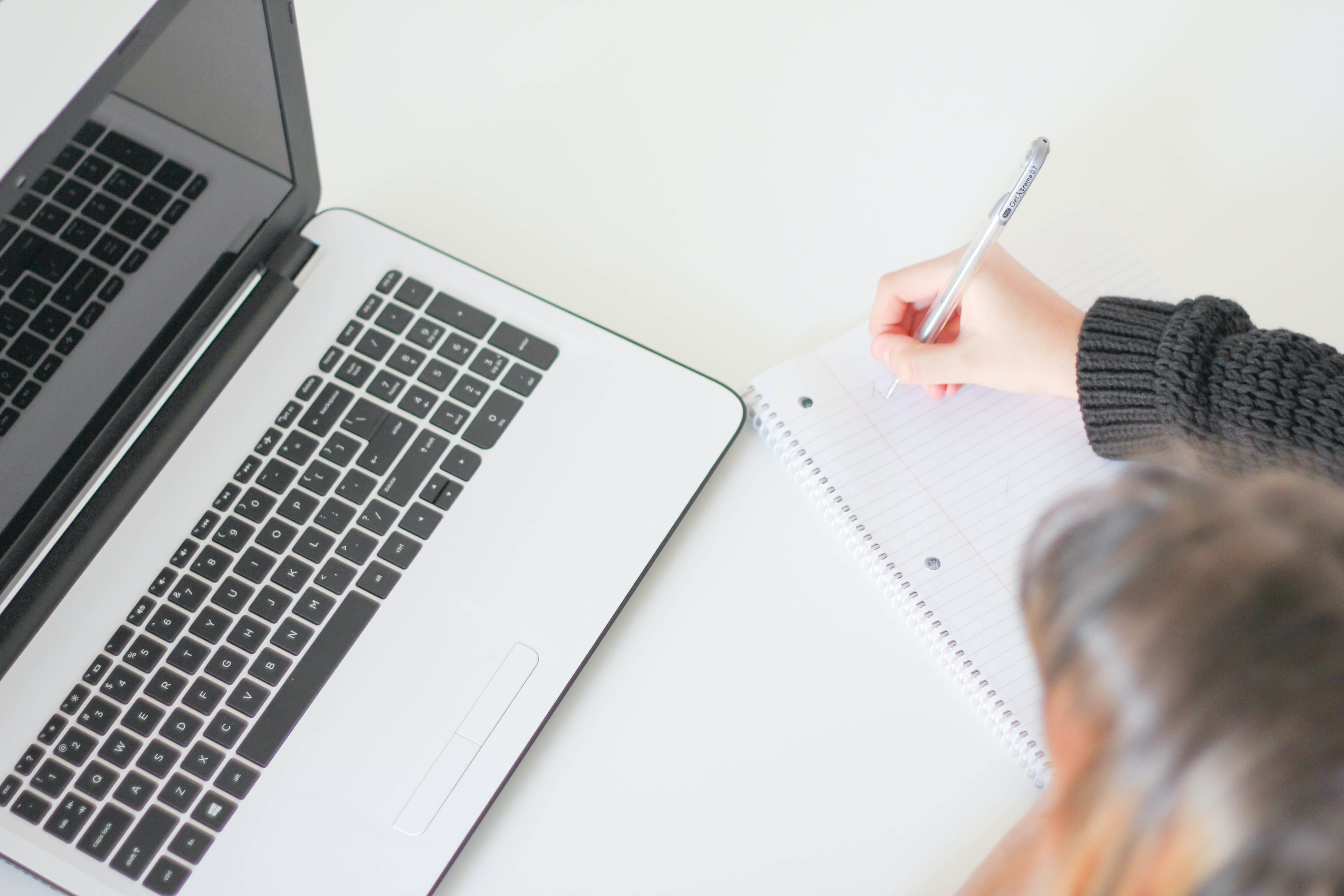 Student writing in a notebook next to a laptop computer.