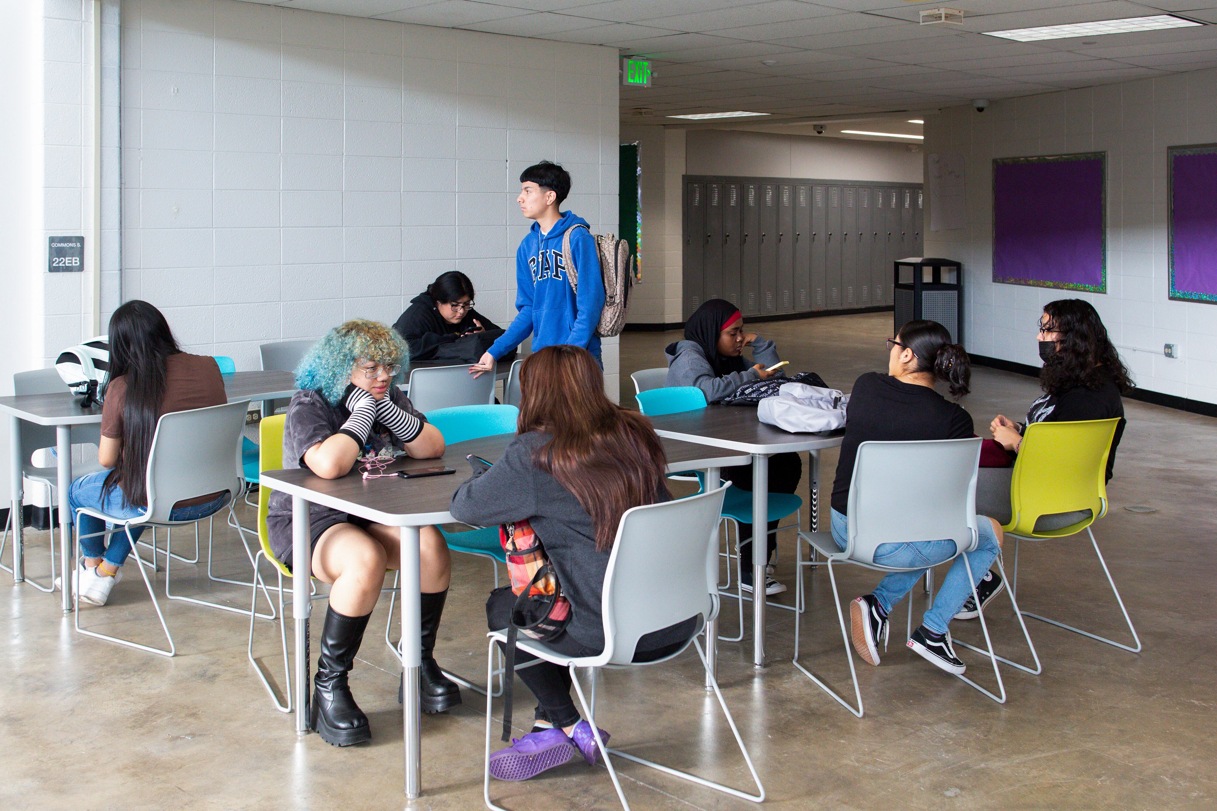 High school students sit at tables in a hallway.