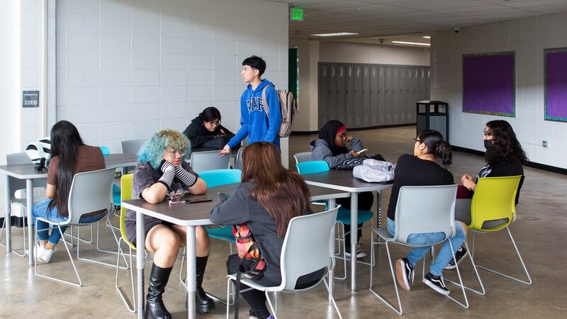 High school students sit at tables in a hallway.