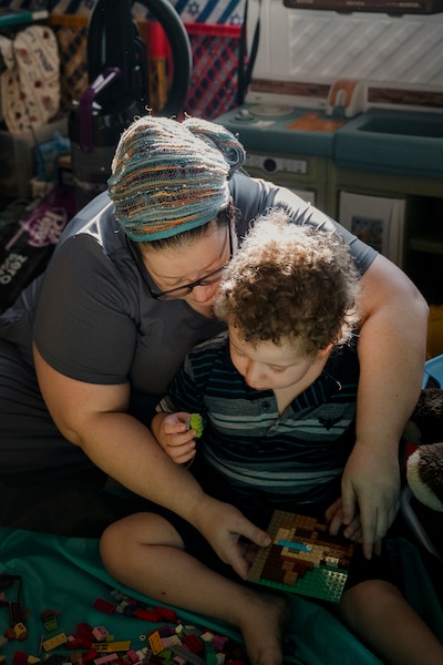 A photograph of a mom embracing her son while sitting on the floor of their home playing with toys.