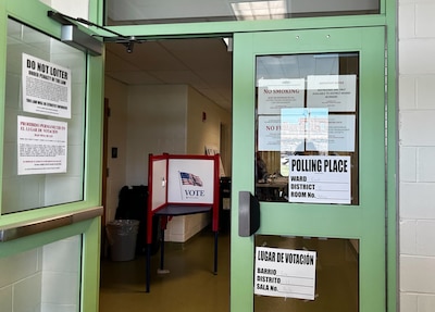 An open green door with voting information taped on.